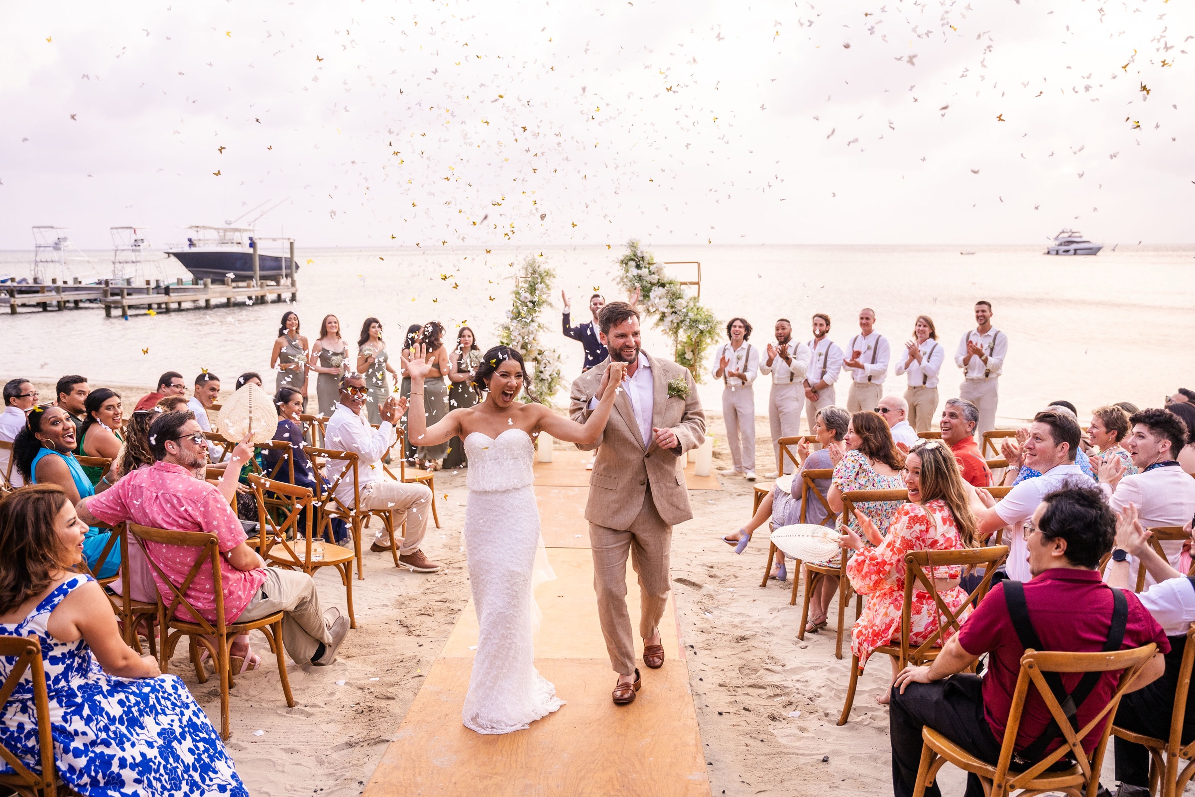 The newlyweds walking through confetti between rows of guests